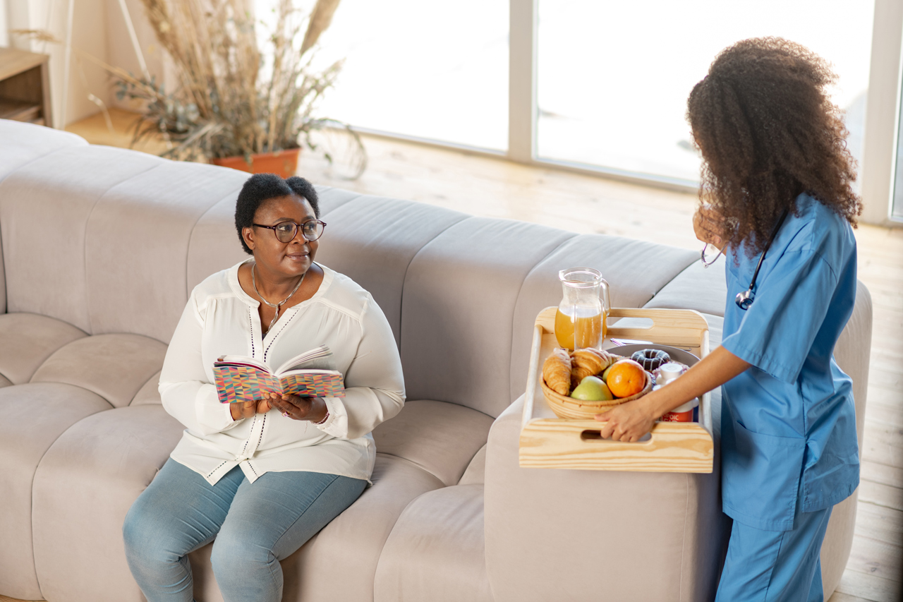 nurse-bringing-croissants-and-fruits-for-aged-lady-sitting-on-sofa-1